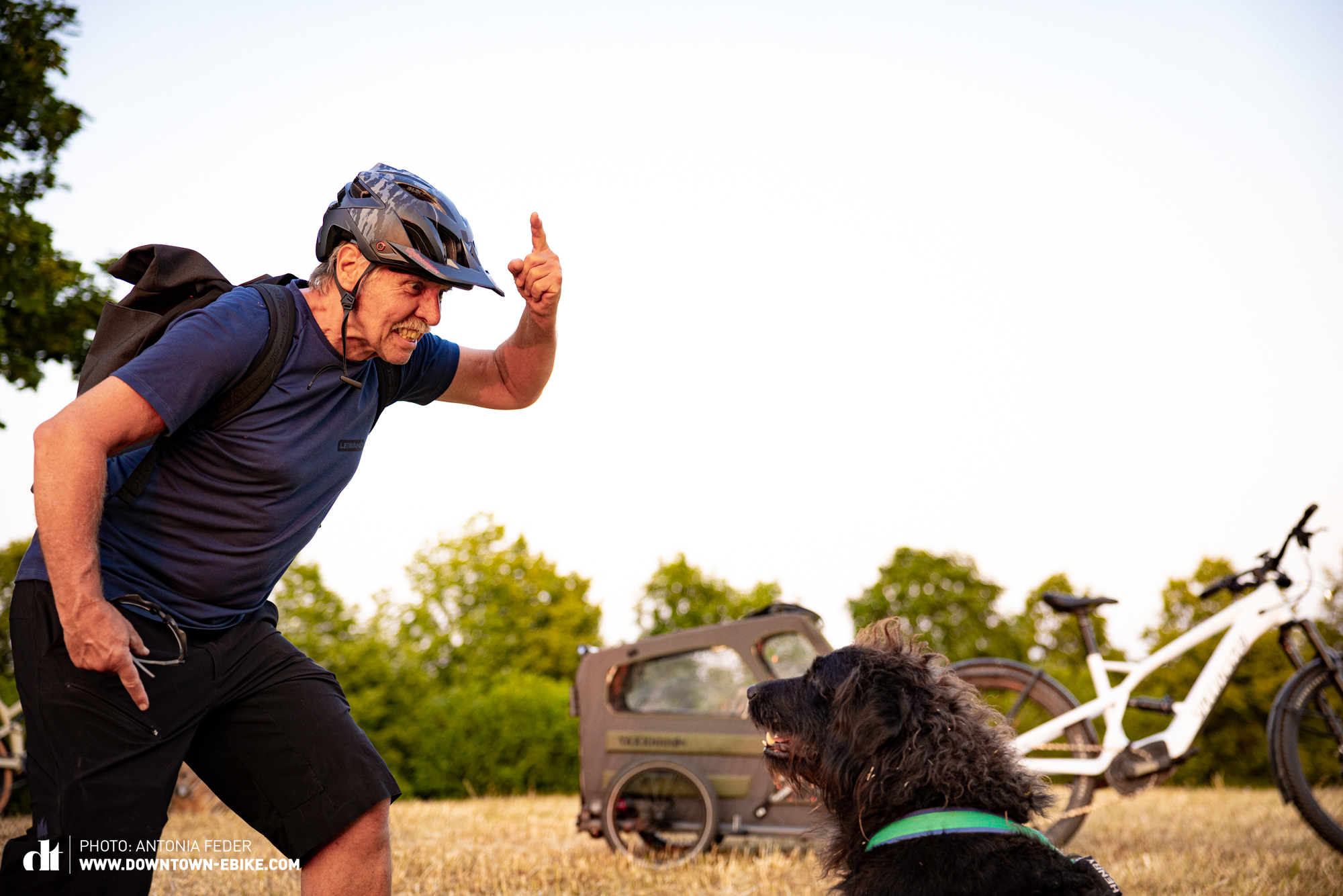 Manne steht mit erhobenen Finger vor seinem Hund Herny und schaut wütend, da dieser nicht in den Fahrrad-Hundeanhänger geht. 